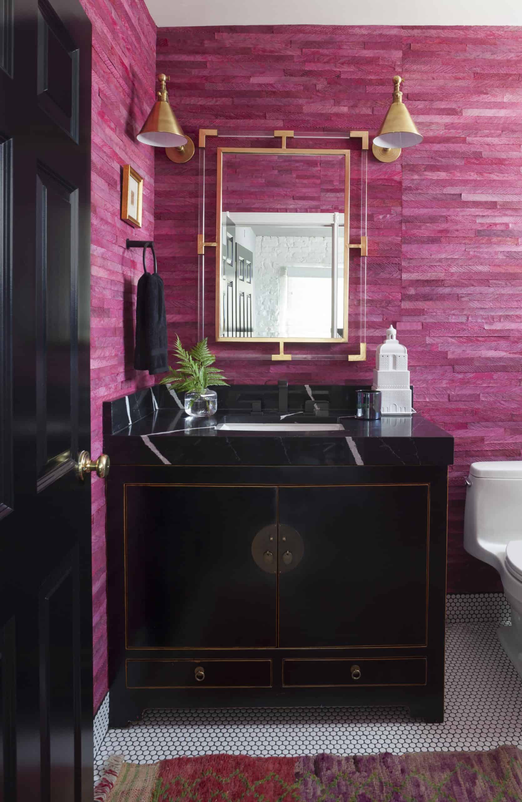 Designer powder room with pink wood wallcovering, brass sconces and beautiful black vanity