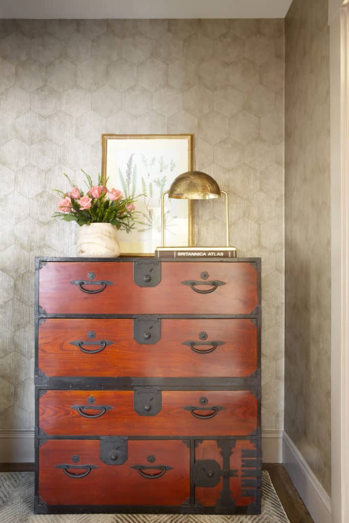 Gorgeous wallpaper in home entry with trunk style dresser