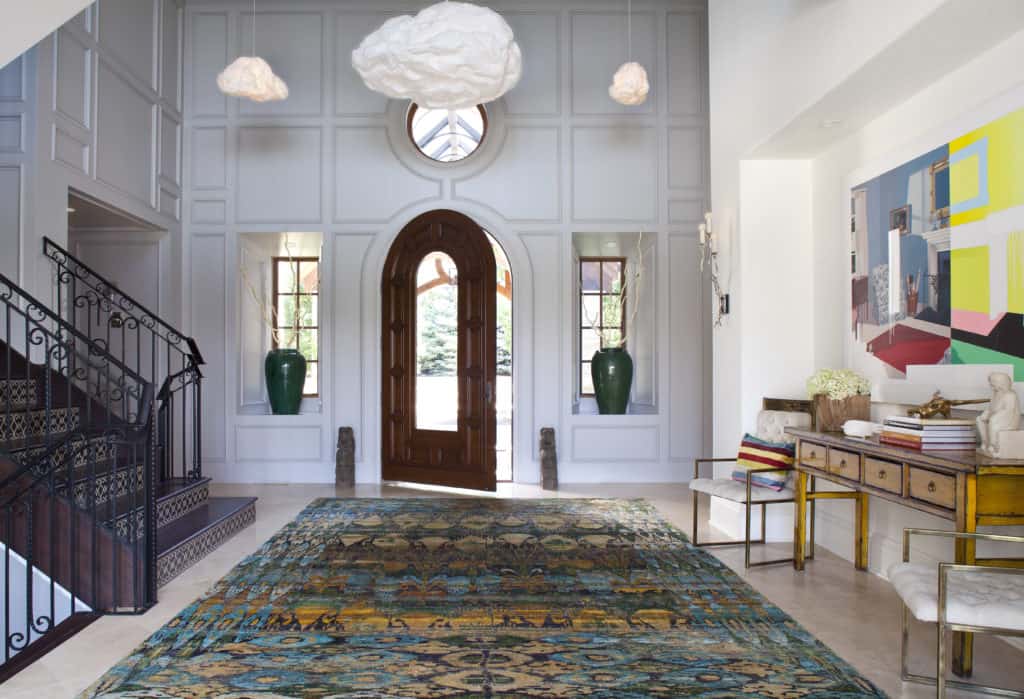 Revamped entry way with white wall panels, metal staircase rails, colorful art and cloud pendants