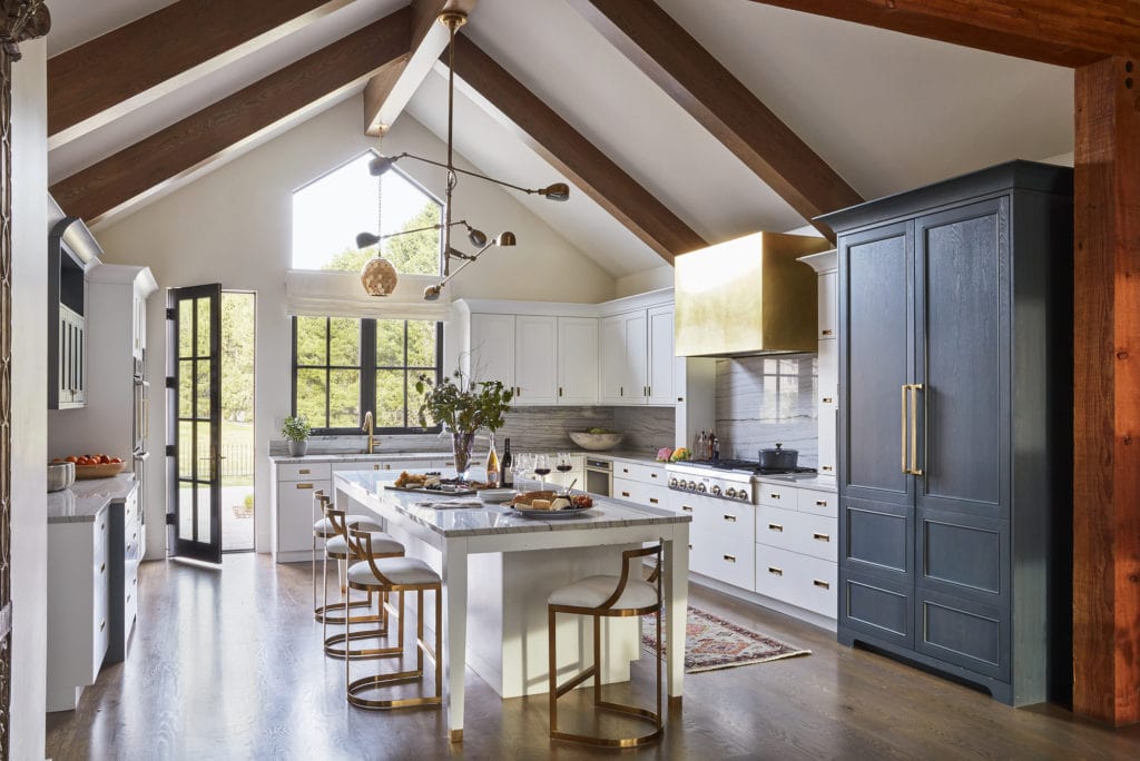 Bright and modern kitchen renovation with white countertops and white cabinets. Brass range hood and exposed beams on the ceilings.