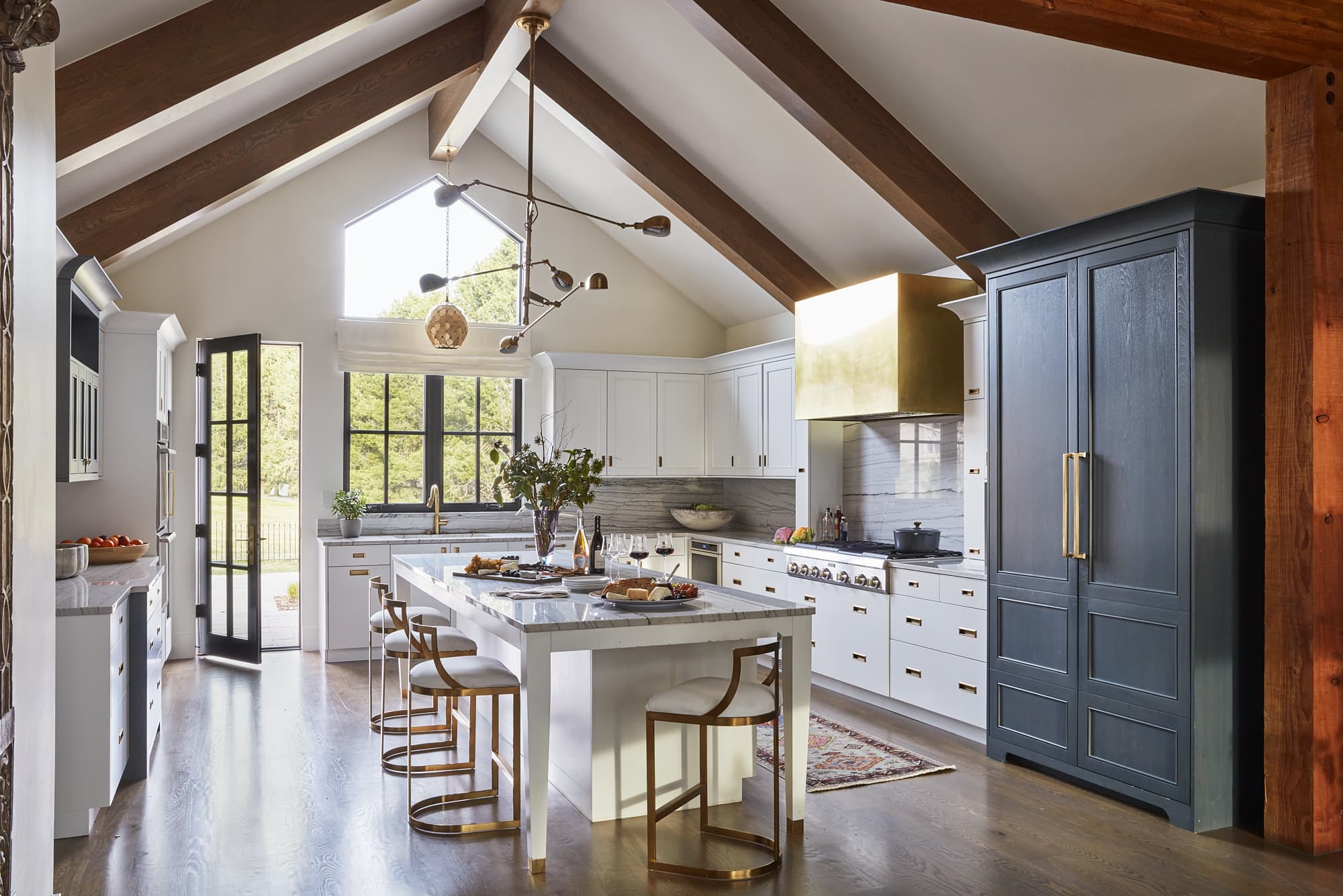 Bright and modern kitchen renovation with white countertops and white cabinets. Brass range hood and exposed beams on the ceilings.