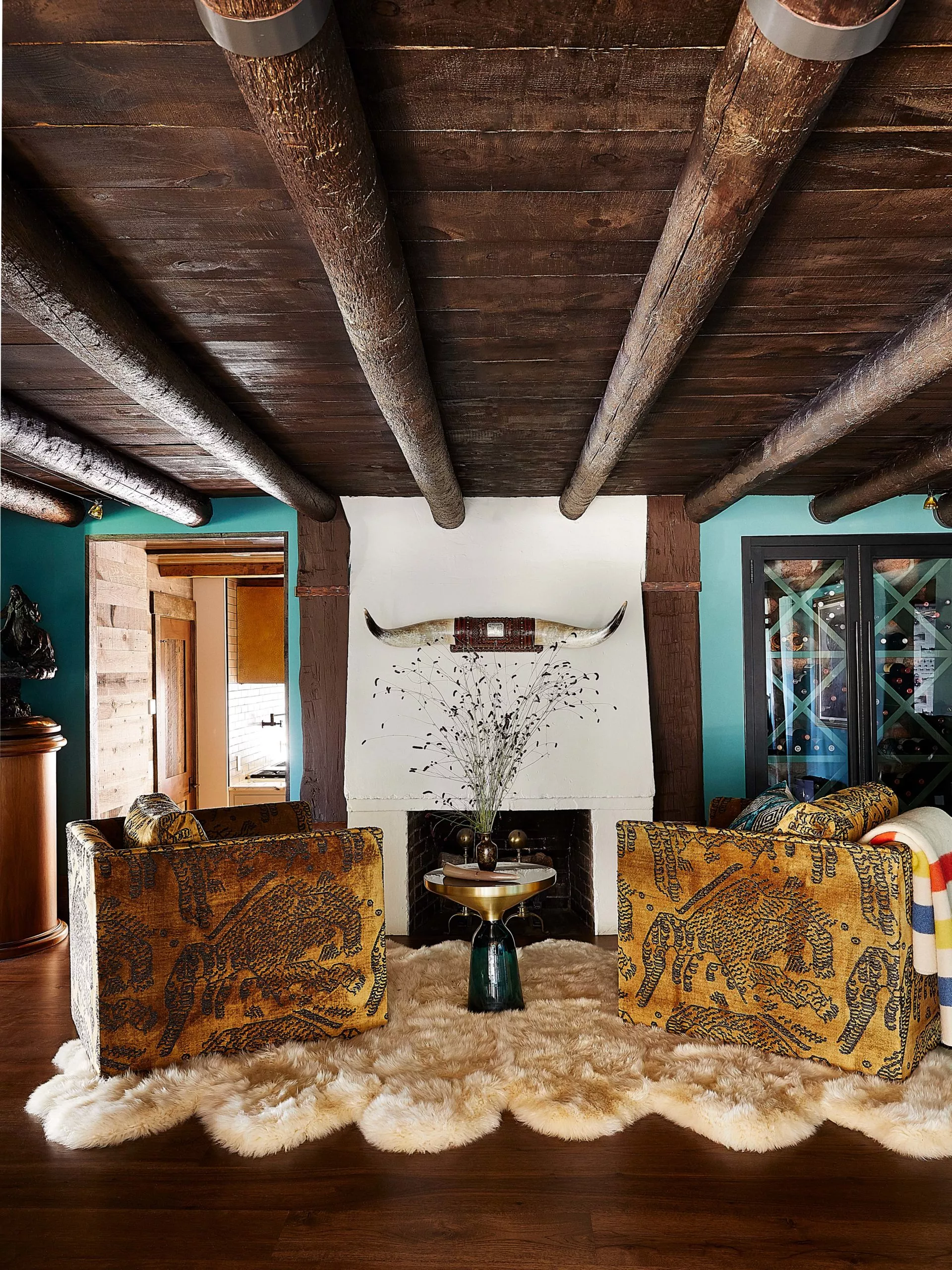 rustic farmhouse interior design stucco fireplace with large sheepskin rug, custom upholstered tiger chairs and log cabin ceilings.